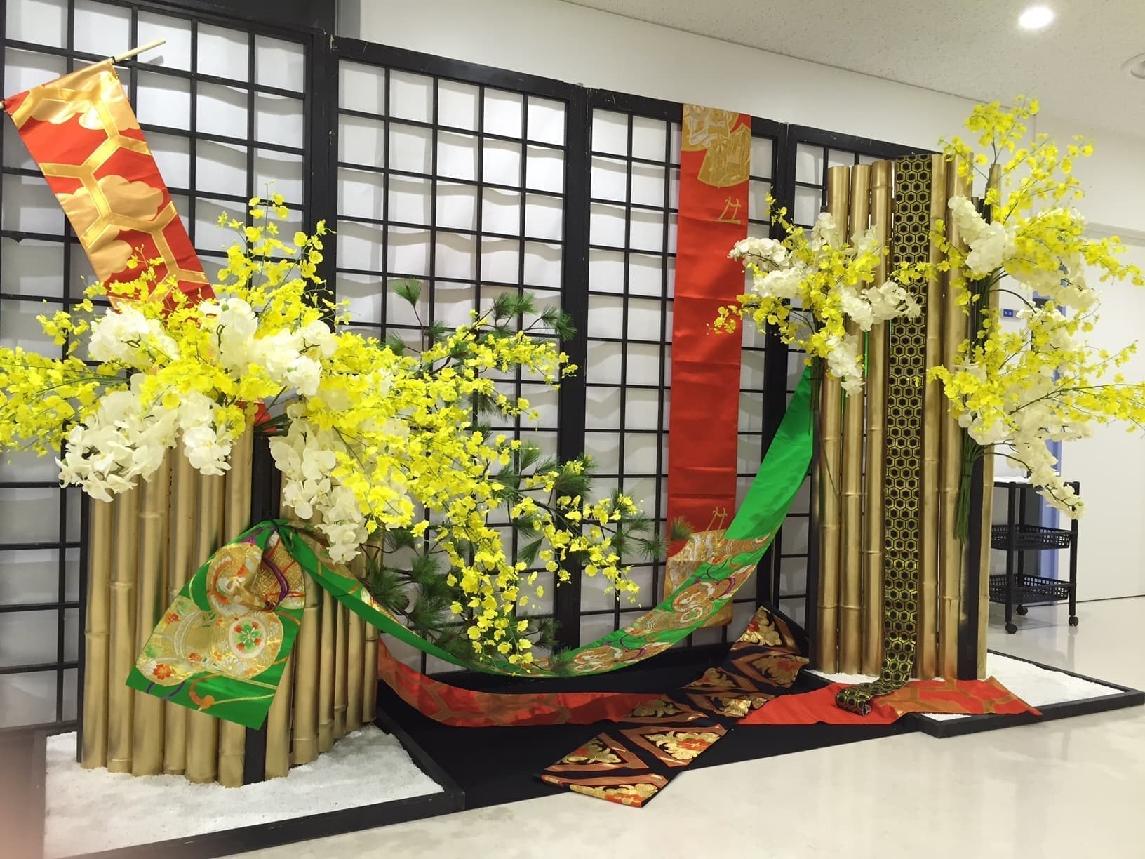 和風ディスプレイ装飾｜金色の竹とアーティフィシャルフラワー（オンシジウム・胡蝶蘭）を使った正月・迎春向け装飾。和柄の帯や黒格子パネルで上品に演出。