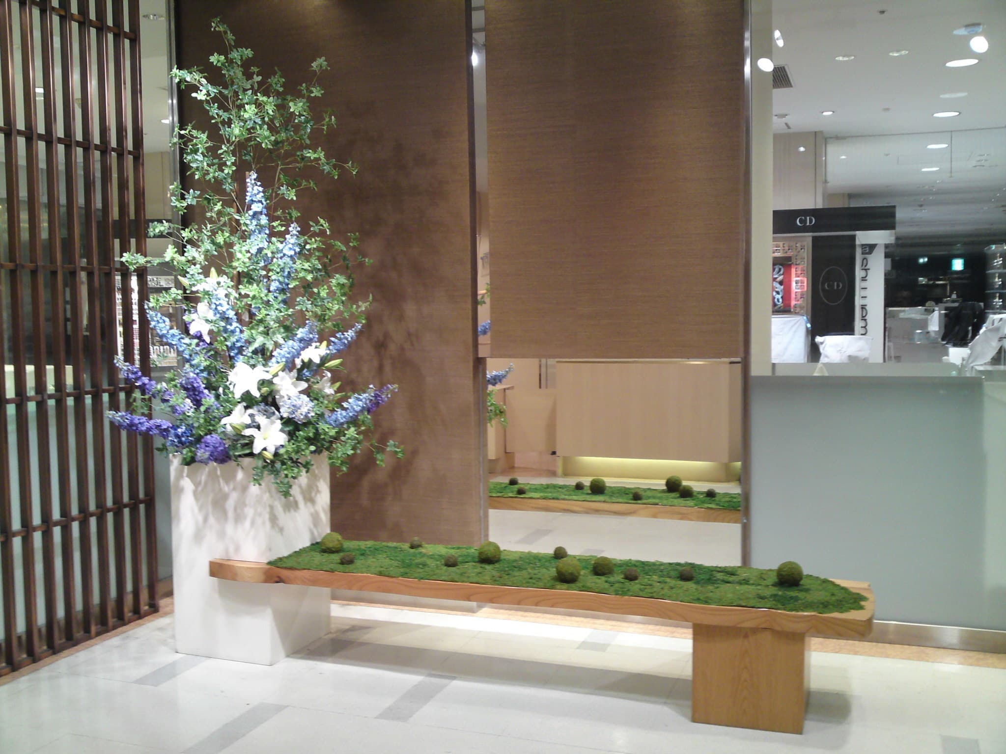 苔とさわやかなブルー系のお花を中心に組み合わせた和モダンなディスプレイ装飾。陶器プランターと木製ベンチを使った高級感のある店舗・ロビー向け演出。